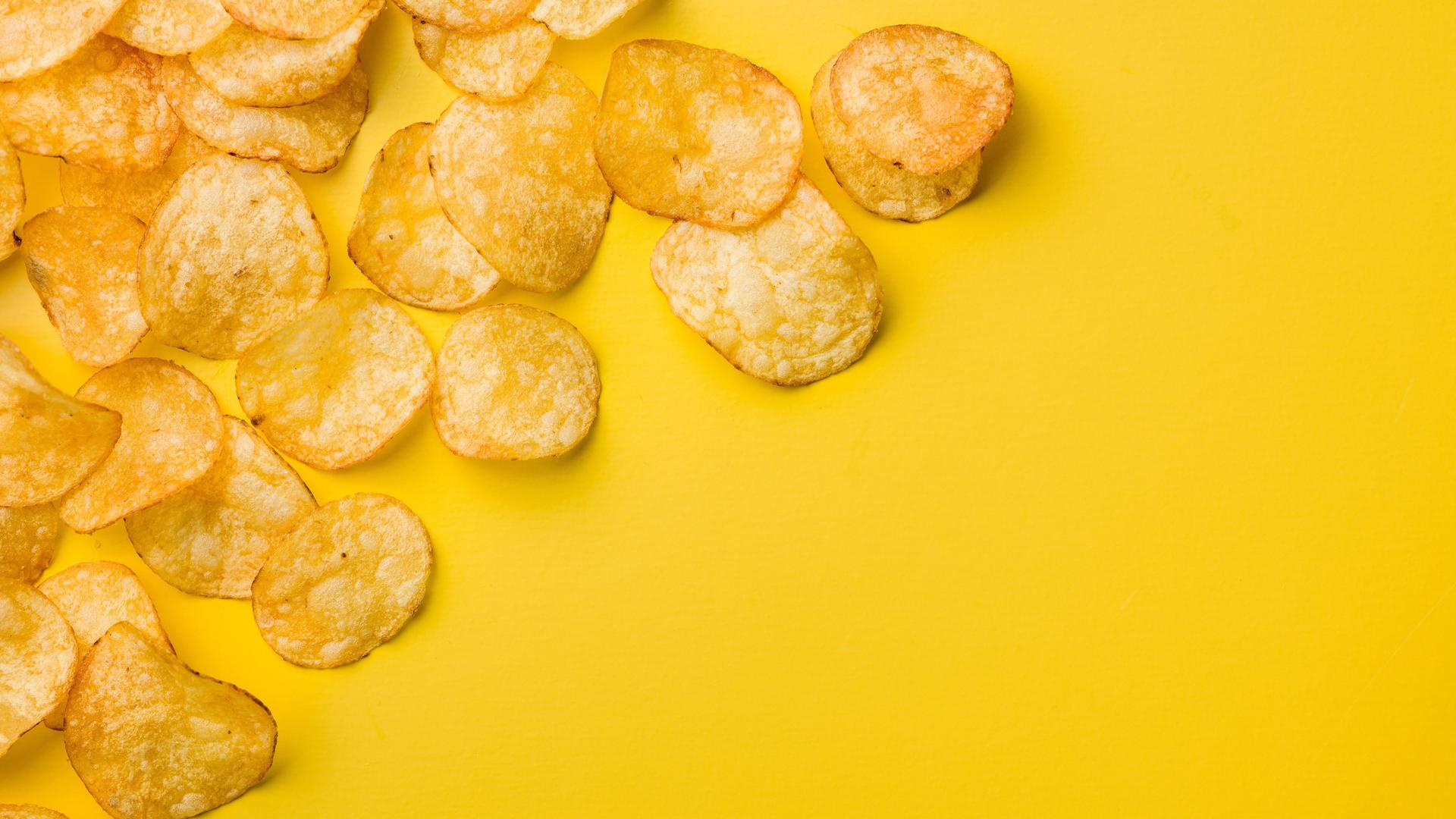 Eine Handvoll Kartoffelchips liegen auf einem gelben Tisch.