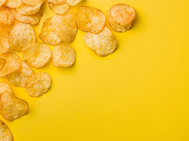 Eine Handvoll Kartoffelchips liegen auf einem gelben Tisch.