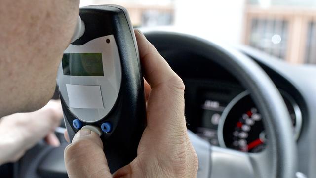 Ein Mann sitzt in einem Auto am Lenkrad und pustet in ein Gerät.