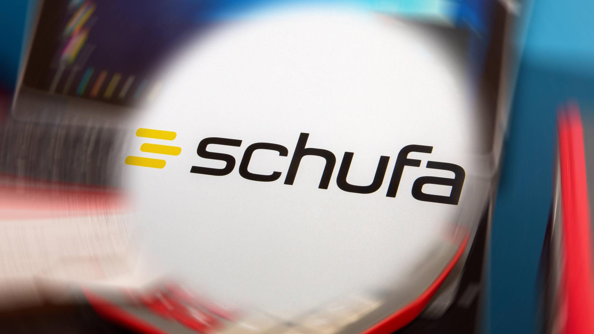 Symbolbild SchufaAuskunft: Schufa-Logo vor einem Schreibtisch mit Tablet, Taschenrechner und Kontoauszügen