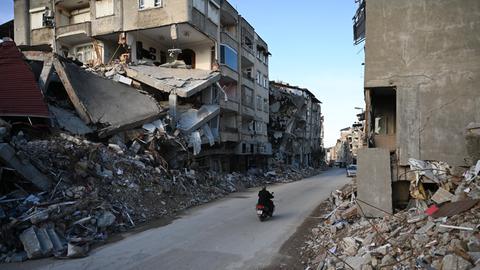Ein Motorrad fährt durch eine Straße in Hatay, die vom Schutt eingestürzter Gebäude gesäumt ist.