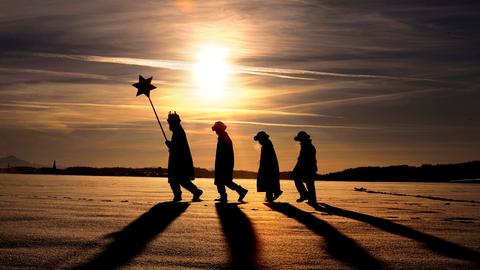 Vier Sternsinger laufen durch die verschneite Landschaft, im tiefstehenden Abendsonnen werfen sie lange Schatten. (Katholische Gemeinde Hl. Familie Kaufbeuren)