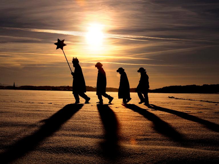 Vier Sternsinger laufen durch die verschneite Landschaft, im tiefstehenden Abendsonnen werfen sie lange Schatten. (Katholische Gemeinde Hl. Familie Kaufbeuren)