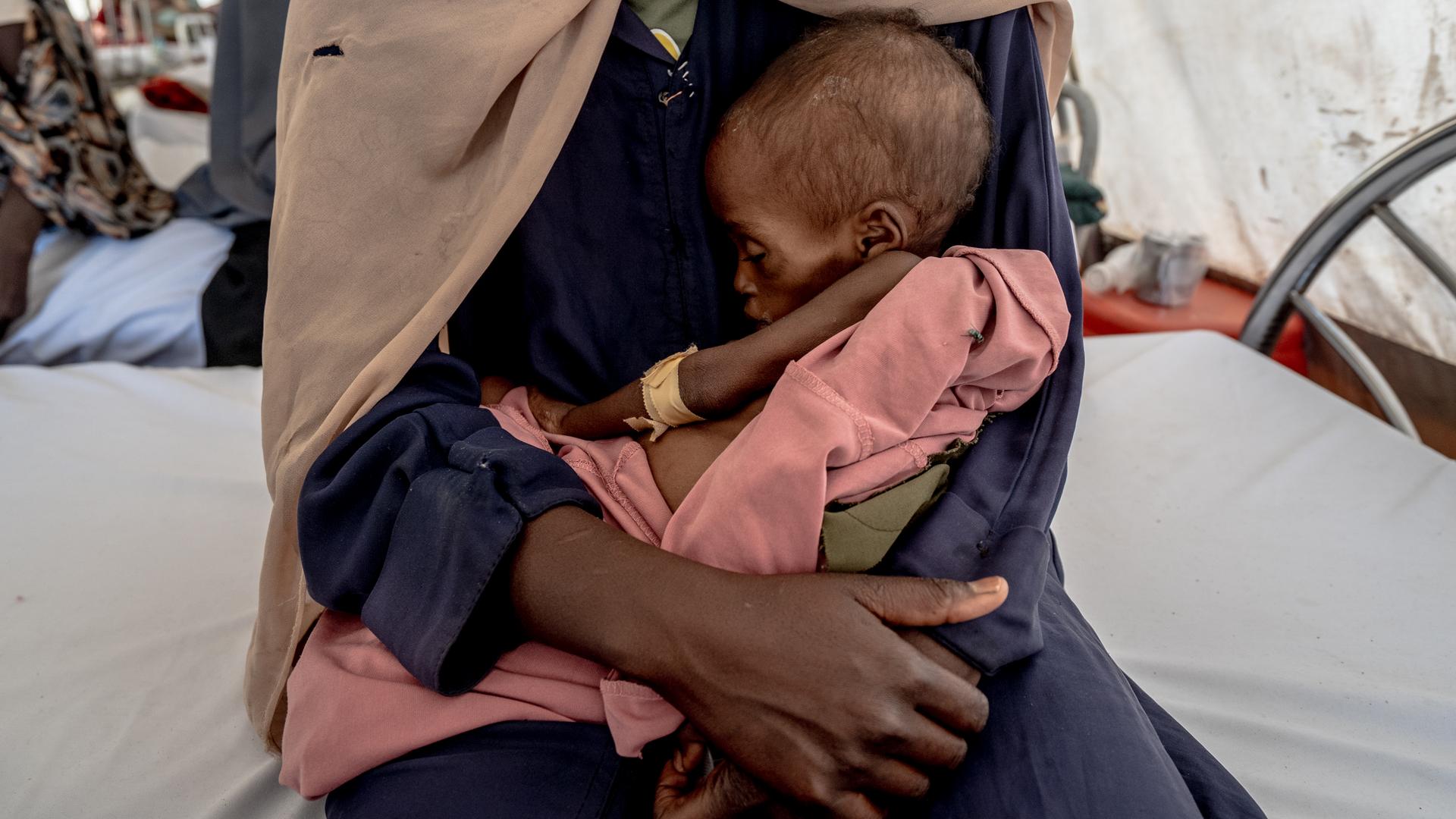 Ein dreijähriges Kind das 5,3 Kilogramm wiegt liegt in den Armen der Mutter auf einer Station für unterernährte Kinder im „Paris-Krankenhaus“ von Ärzte ohne Grenzen in Tawila in einem Flüchtlingslager im Sudan.
