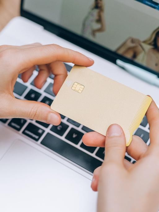 Eine Frau hält eine Kreditkarte in der Hand während sie im Netz shoppt.
