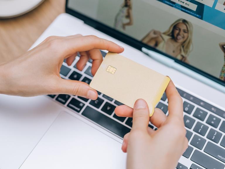 Eine Frau hält eine Kreditkarte in der Hand während sie im Netz shoppt.