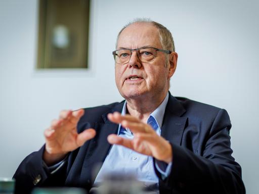 Peer Steinbrück, Bundesminister a.D., SPD, gestikuliert während eines Interviews mit den Händen, im Hintergrund sieht man verschwommen ein Bild an der Wand.