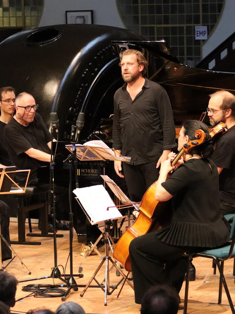 Ein Streichquartett, ein Pianist am Flügel und ein stehender Sänger auf einer Bühne in Konzertsituation. Alle sind schwarz gekleidet, im Hintergrund sieht man den historischen Raum mit einer stillgelegten Turbine. 