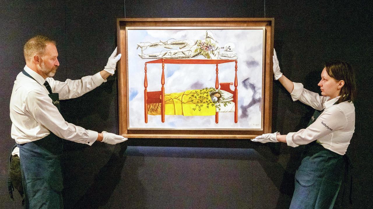 Ein Mann und eine Frau halten ein Gemälde von Frida Kahlo. Es zeigt eine Frau in einem Bett.