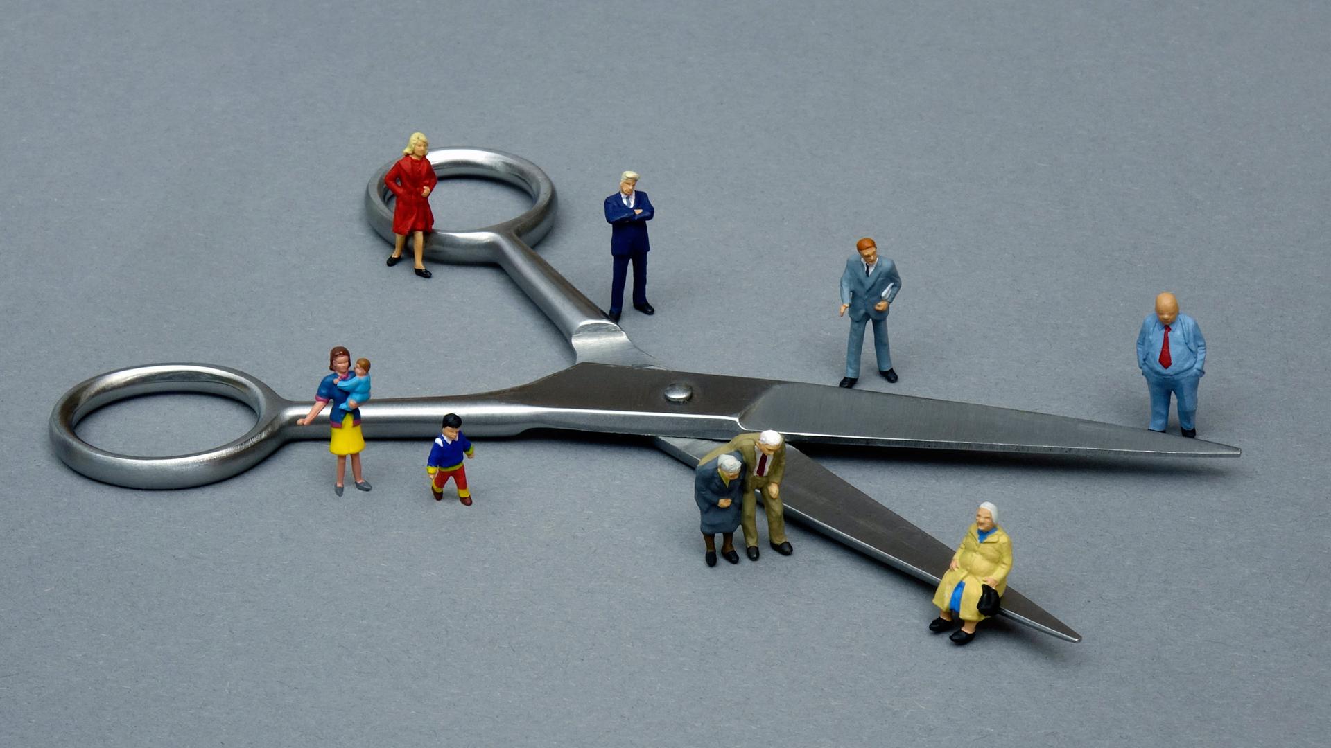 Ein Symbolbild zeigt um eine Schere gruppierte kleine Figuren, um so die Teilung der Gesellschaft zu veranschaulichen.