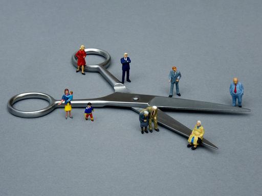 Ein Symbolbild zeigt um eine Schere gruppierte kleine Figuren, um so die Teilung der Gesellschaft zu veranschaulichen.