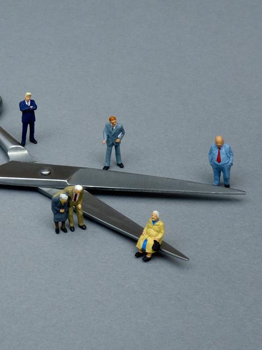 Ein Symbolbild zeigt um eine Schere gruppierte kleine Figuren, um so die Teilung der Gesellschaft zu veranschaulichen.