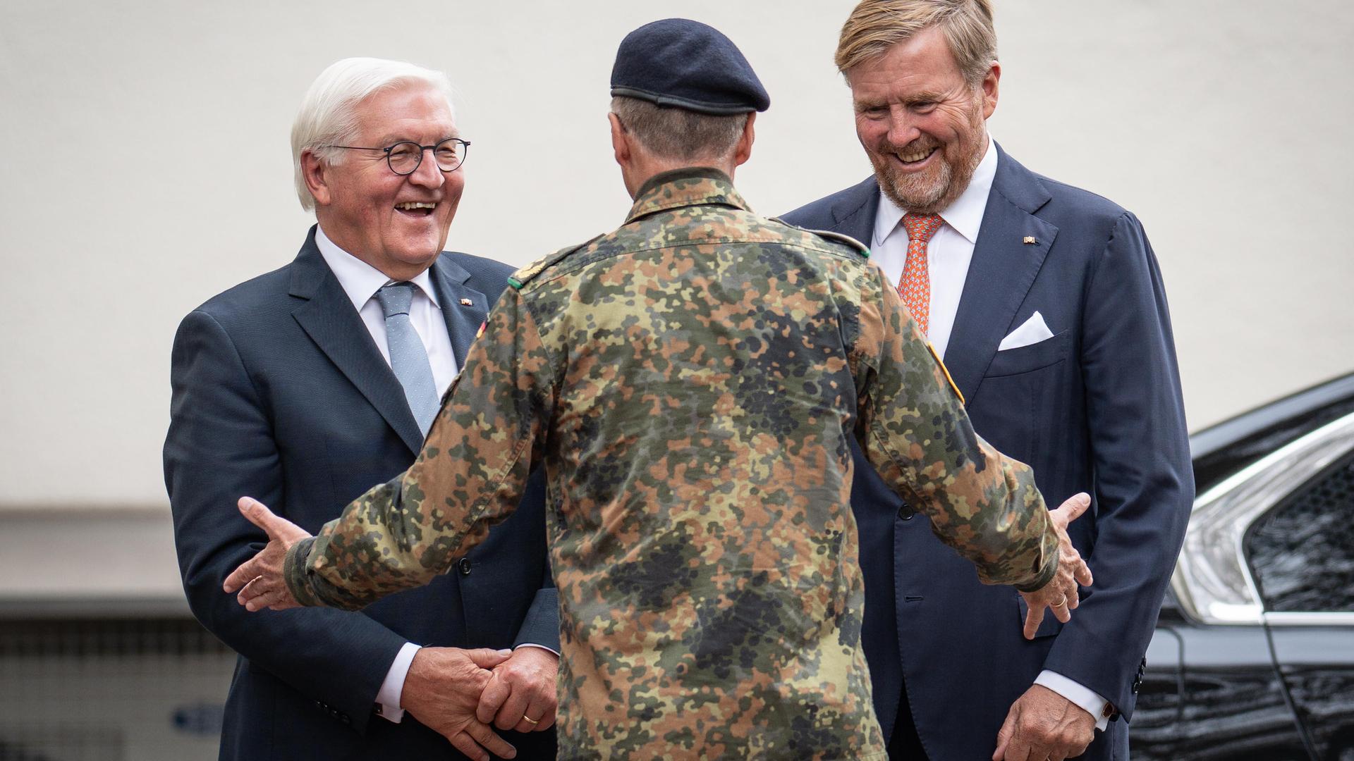 Steinmeier und Willem-Alexander stehen mit lächelnden Gesichtern vor einem Bundeswehr-Vertreter, der den beiden militärisches Gerät erklärt.