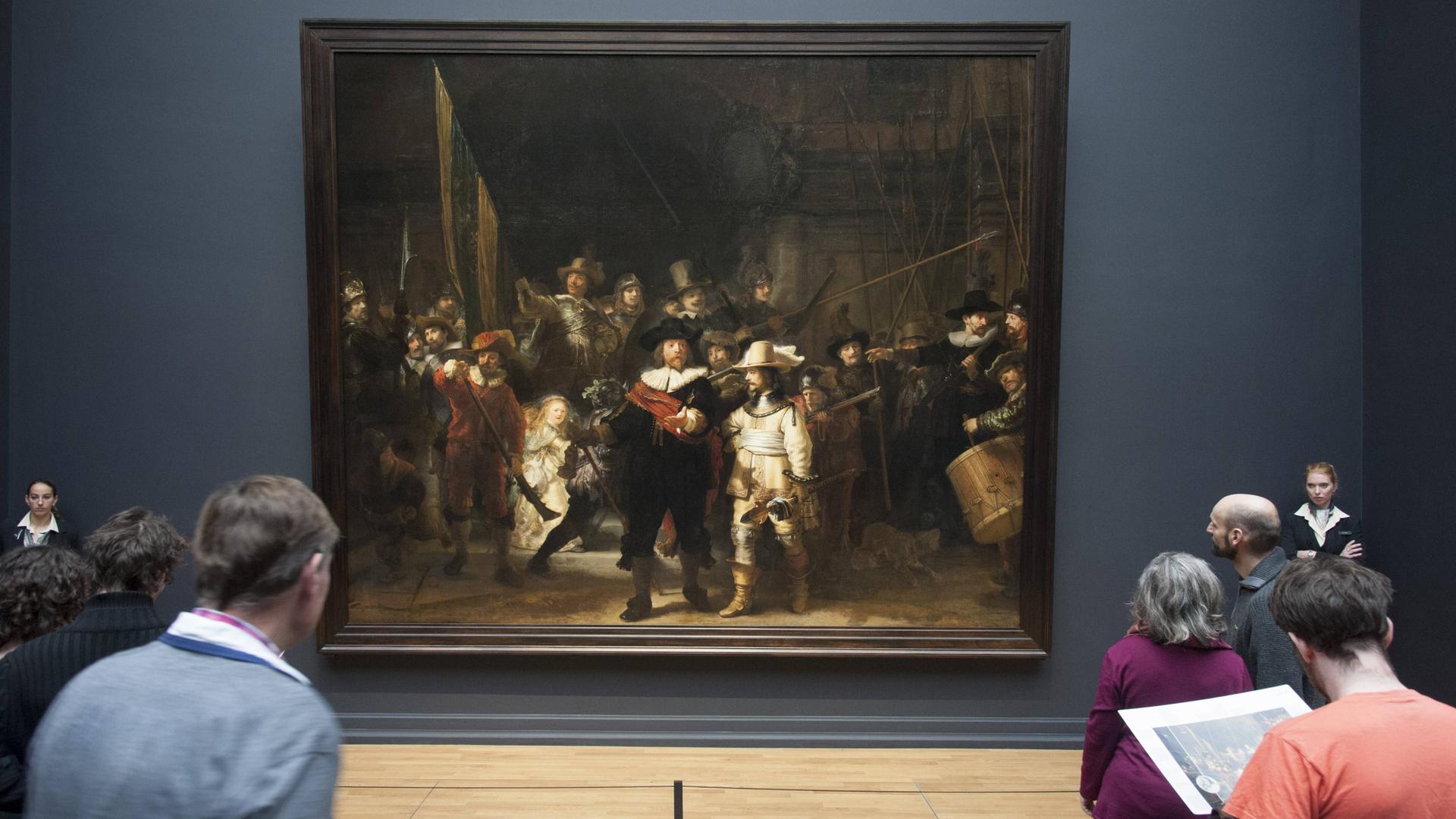 Besucher stehen vor dem von zwei Museumswächtern bewachten Gemälde "Die Nachtwache" von Rembrandt im Rijksmuseum in Amsterdam in den Niederlanden.