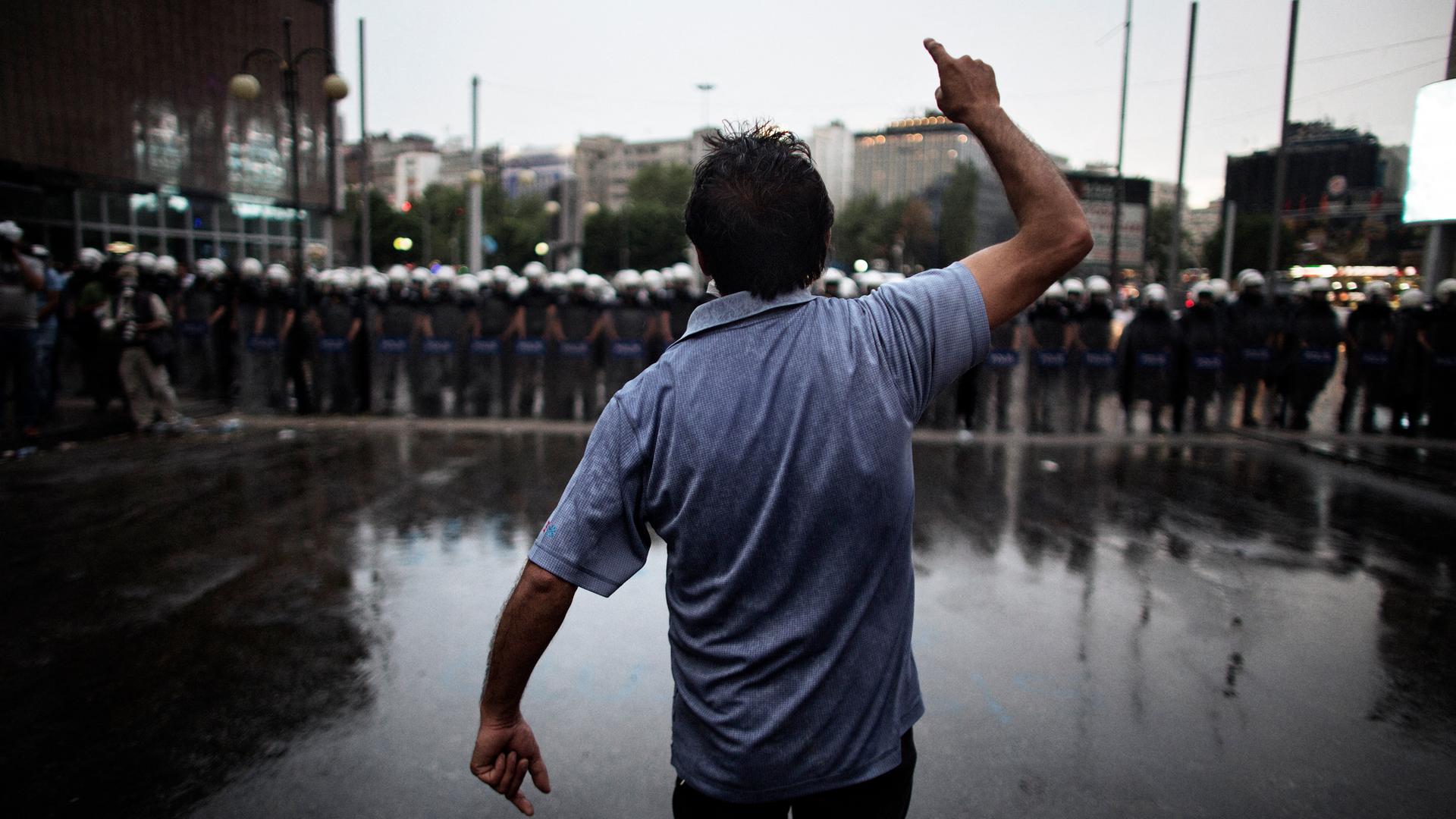 Ein gestikulierender Mann steht auf dem Taksim-Platz einer Reihe schwer uniformierter und bewaffneter Polizisten gegenüber. Man sieht die Person von hinten.