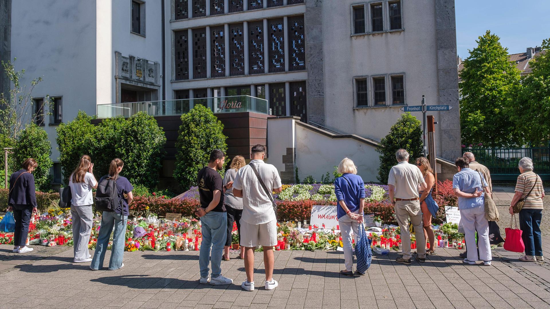 Menschen in Trauer und Gedenken stehen vor Blumen und Kerzen an der Stadtkirche in der Solinger Innenstadt