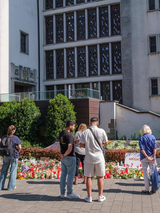 Menschen in Trauer und Gedenken stehen vor Blumen und Kerzen an der Stadtkirche in der Solinger Innenstadt