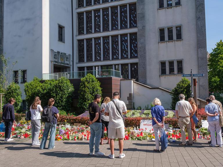 Menschen in Trauer und Gedenken stehen vor Blumen und Kerzen an der Stadtkirche in der Solinger Innenstadt