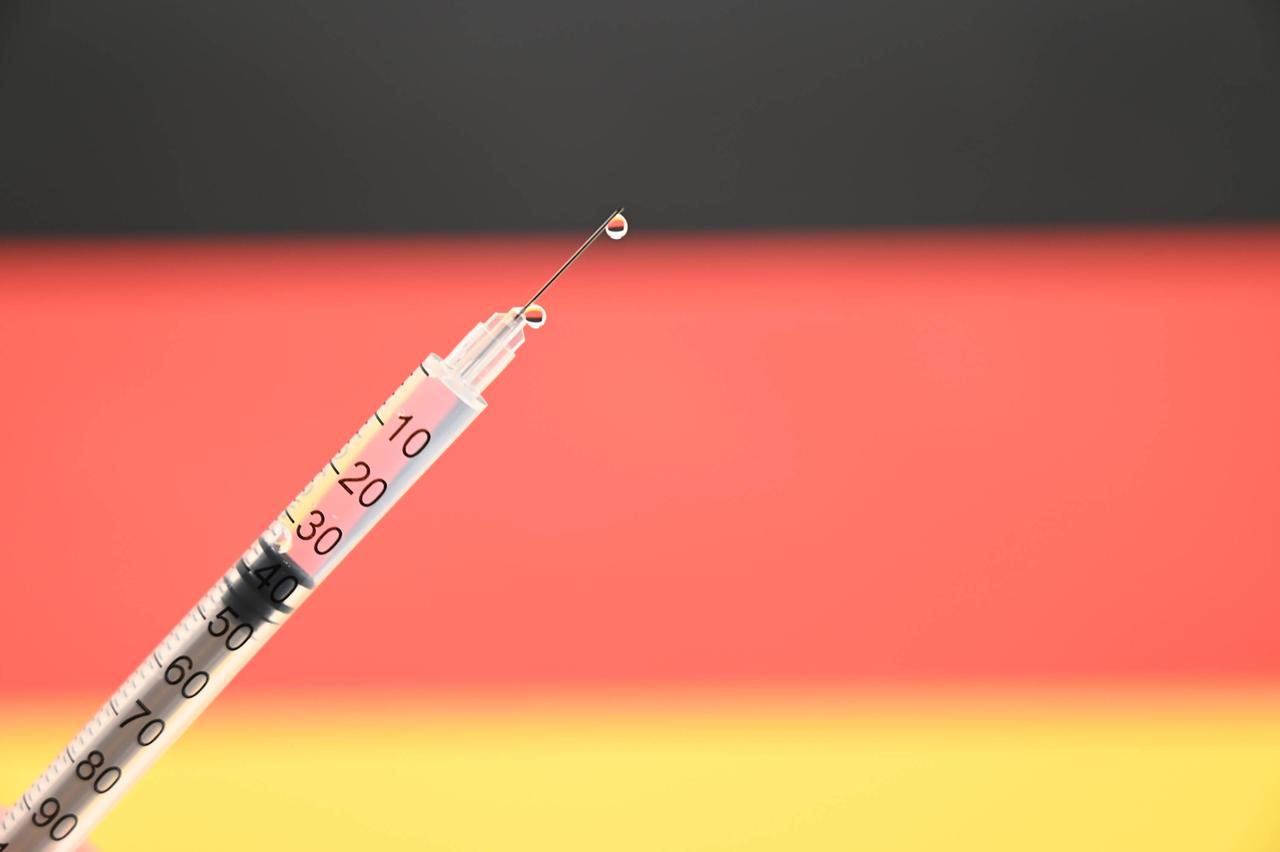 Eine Impfspritze vor einer nur unscharf zu sehenden Deutschland-Fahne