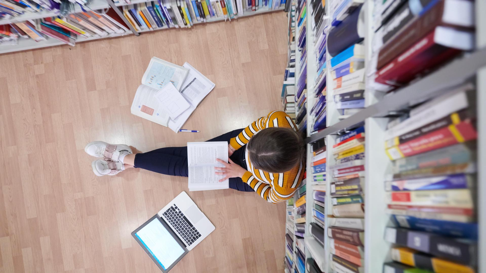 Studentin sitzt in einer Bibliothek auf dem Boden. Studentin sitzt in einer Bibliothek auf dem Boden.