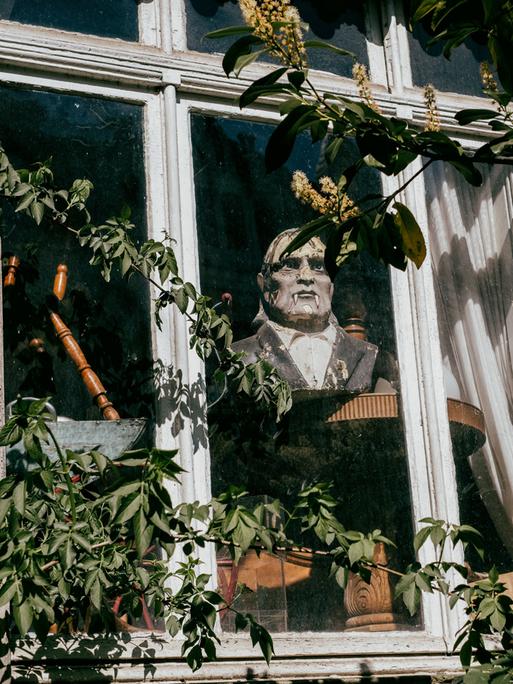 Graf-Dracula-Statue blickt aus dem verschlossenen Fenster eines alten Gebäudes.