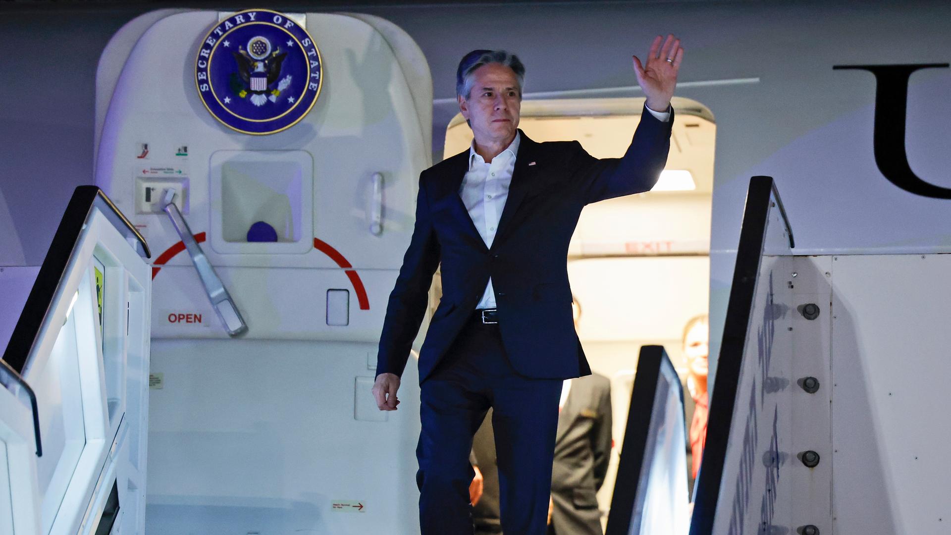 US-Außenminister Blinken winkt aus der geöffneten Tür eines Flugzeugs.