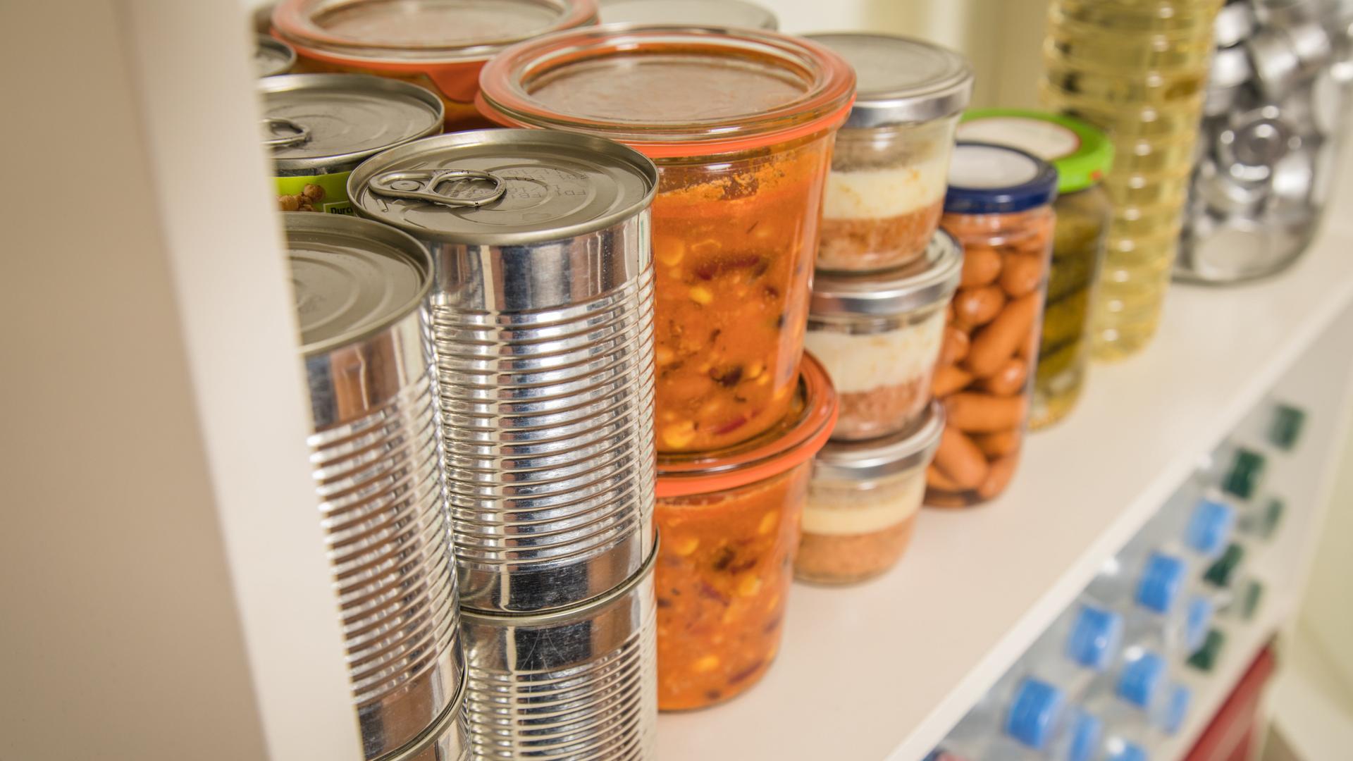 Verschiedene Vorräte wie Dosen, Gläser und Wasserflaschen stehen in einem Regal Verschiedene Vorräte wie Dosen, Gläser und Wasserflaschen stehen in einem Regal