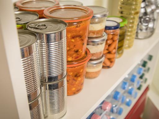 Verschiedene Vorräte wie Dosen, Gläser und Wasserflaschen stehen in einem Regal