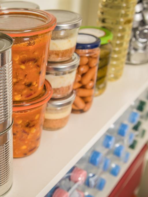 Verschiedene Vorräte wie Dosen, Gläser und Wasserflaschen stehen in einem Regal