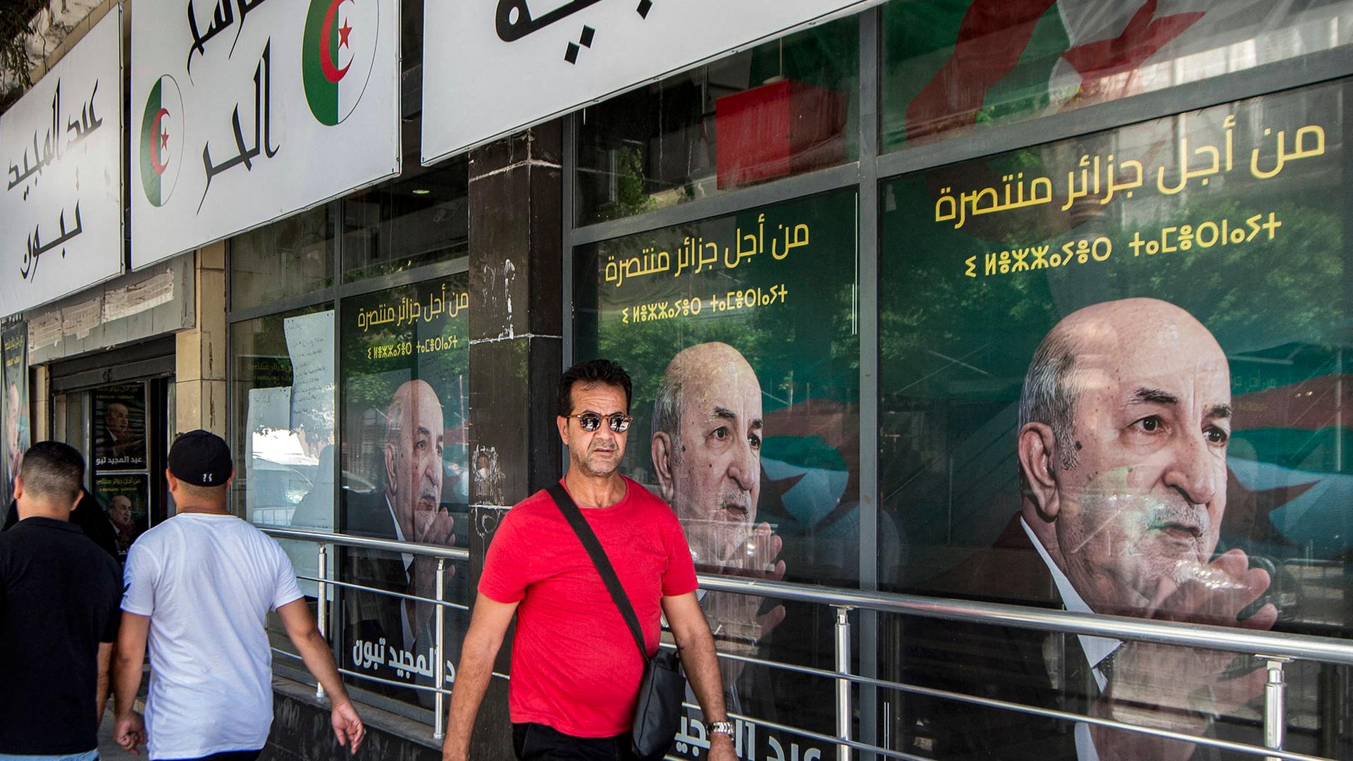 Menschen laufen vor dem Büro der Wahlkampagne von Präsident Abdelmajid Tebboune in Algier vorbei.