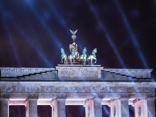 Lichstrahlen leuchten vor dem dunklen Himmel und der Quadriga am Brandenburger Tor.
