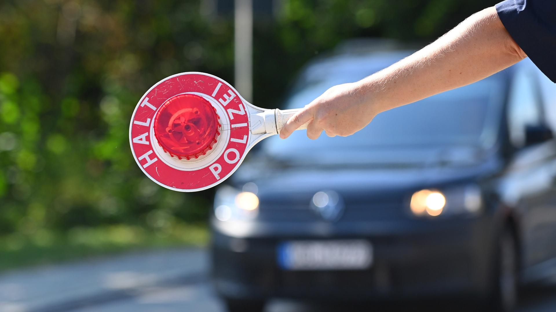 Ein Polizist hält eine Polizeikelle "HALT POLIZEI", Grenzpolizisten kontrollieren Fahrzeuge