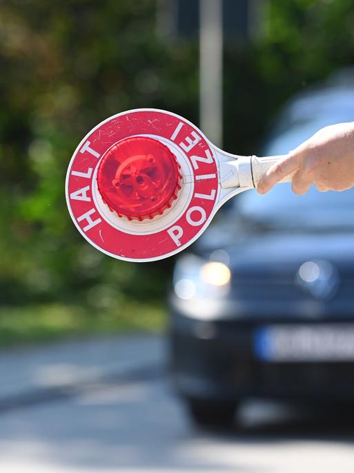 Ein Polizist hält eine Polizeikelle "HALT POLIZEI", Grenzpolizisten kontrollieren Fahrzeuge