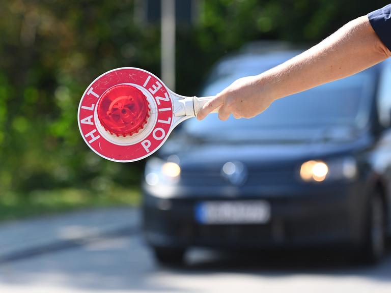 Ein Polizist hält eine Polizeikelle "HALT POLIZEI", Grenzpolizisten kontrollieren Fahrzeuge