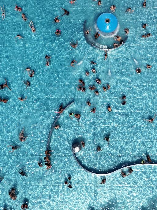 Blick von oben auf das Michaelibad in München, wo Besucher in einem großen Schwimmbecken schwimmen.