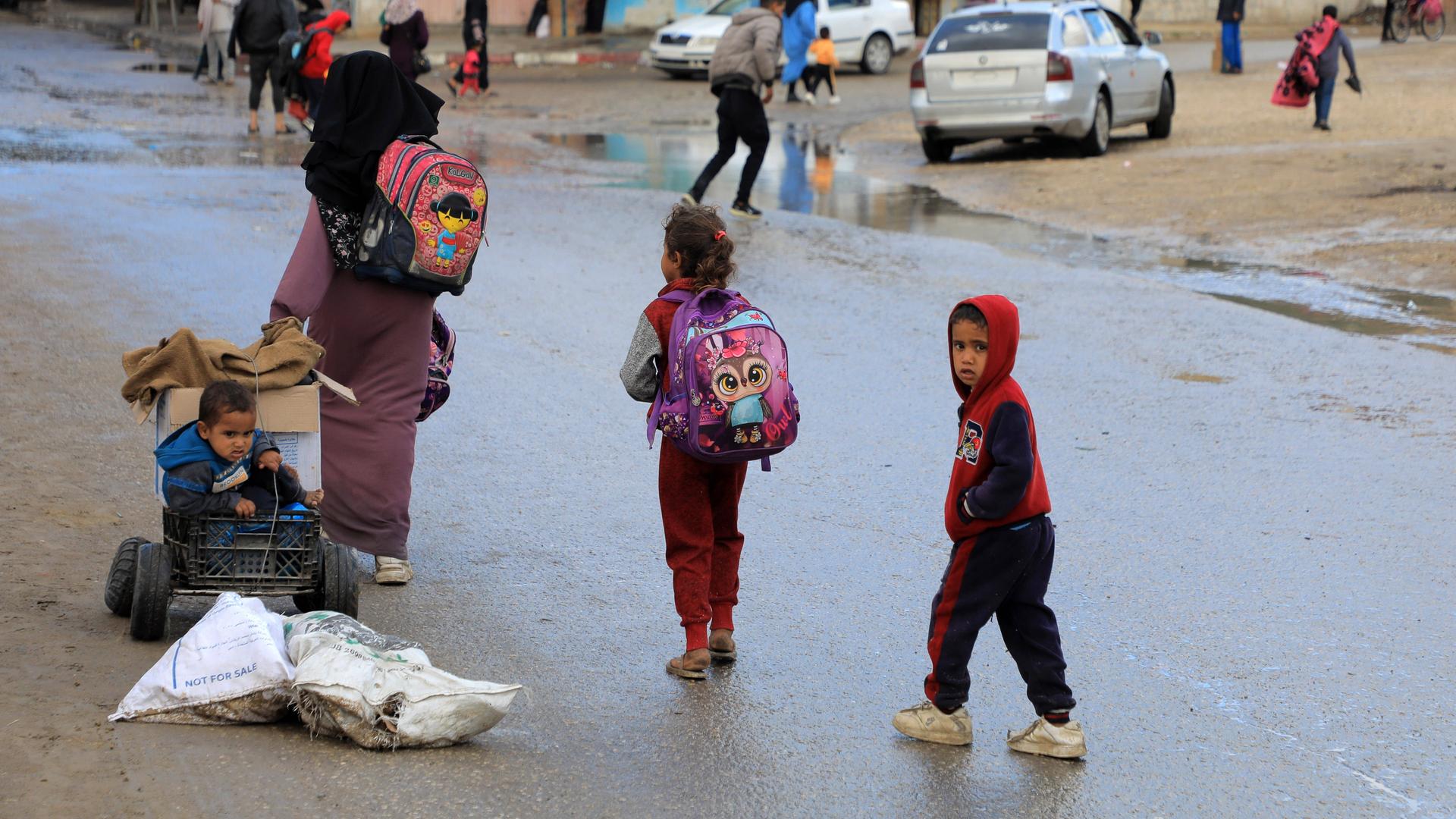 Mehrere Kinder tragen Rucksäcke und gehen über eine nasse Straße.