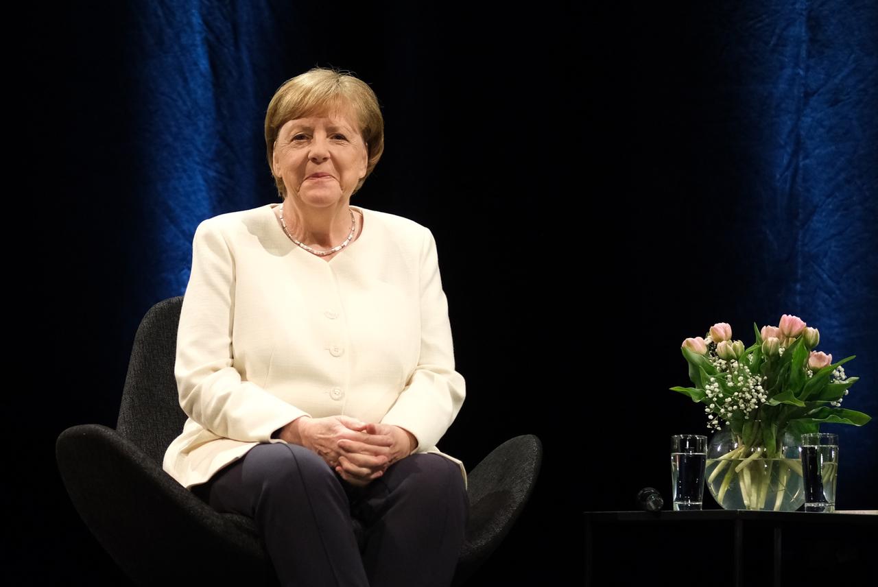 Die frühere Bundeskanzlerin Angela Merkel bei einer Veranstaltung im Rahmen der Leipziger Buchmesse auf einer Bühne im Schauspiel Leipzig. Sie sitzt auf einem Stuhl vor dunklem Hintergrund, neben ihr ein Tischchen mit einem Blumenstrauß.