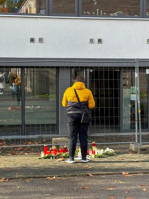 Ein Mann steht vor der eingezäunten der Offenburger Waldbachschule mit Kerzen und Blumen.