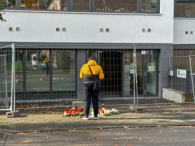 Ein Mann steht vor der eingezäunten der Offenburger Waldbachschule mit Kerzen und Blumen.