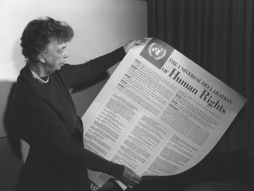 Ein Schwarz-Weiß-Foto zeigt Eleanor Roosevelt, wie sie die Allgemeine Erklärung der Menschenrechte der Vereinten Nationen hält und betrachtet.