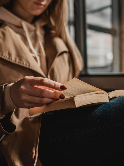 Frau mit hellbraunem Mantel sitzt in einem Zug und liest ein Buch im Zug Frau mit hellbraunem Mantel sitzt in einem Zug und liest ein Buch im Zug