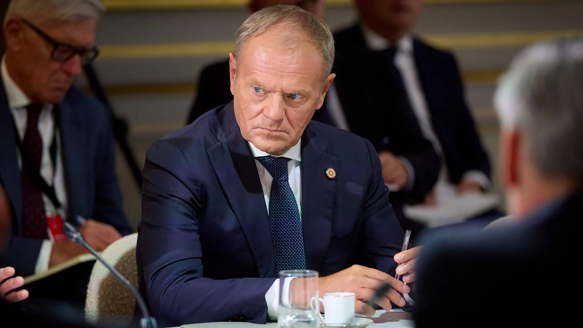 Der polnische Premierministier Donald Tusk sitzt mit weiteren Menschen an einem Konferenztisch. Er blickt sehr ernst.