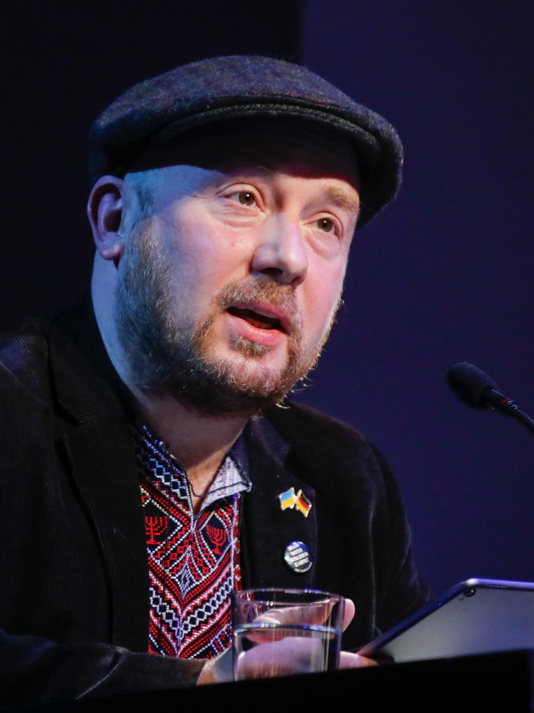 Yuriy Gurzhy sitzt mit Schiebermütze bei "Sprachlos die Sprache verteidigen: Lesung für die Ukraine" im Maxim Gorki Theater vor einem Mikrofon.