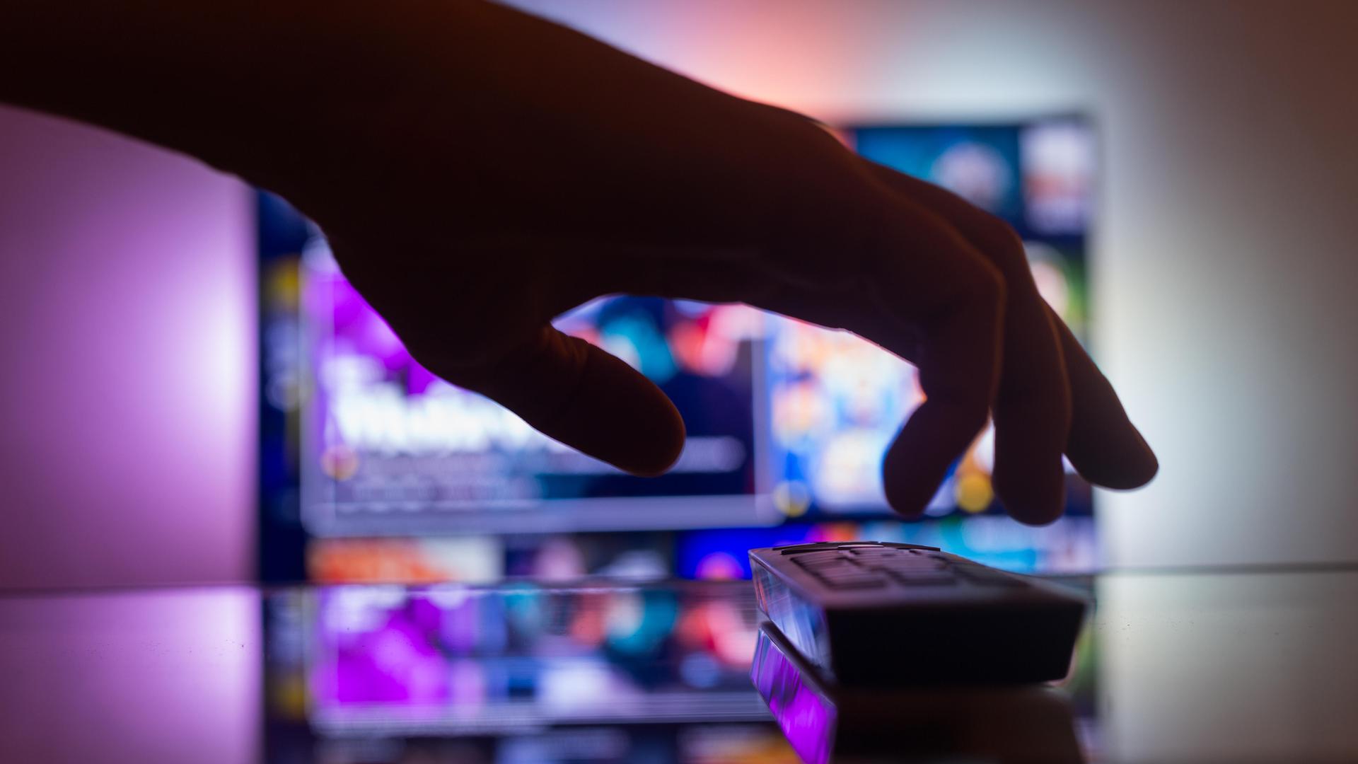 TV mit Streaming mit einer Fernbedienung in der Nähe der Wand im Zimmer. Nachrichten und Serien online. Videos im Fernsehen anschauen. Hand nimmt TV-Fernbedienung