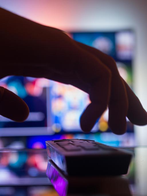 TV mit Streaming mit einer Fernbedienung in der Nähe der Wand im Zimmer. Nachrichten und Serien online. Videos im Fernsehen anschauen. Hand nimmt TV-Fernbedienung