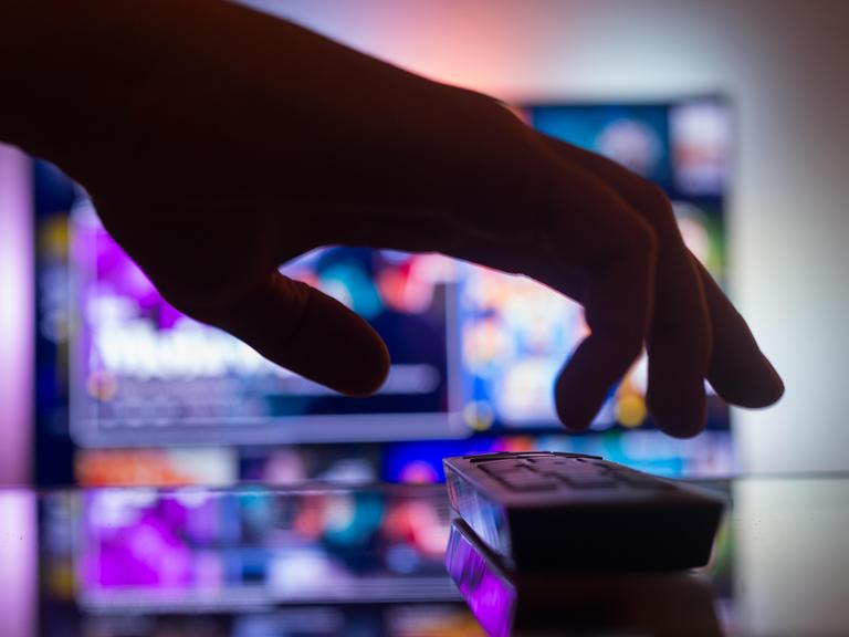 TV mit Streaming mit einer Fernbedienung in der Nähe der Wand im Zimmer. Nachrichten und Serien online. Videos im Fernsehen anschauen. Hand nimmt TV-Fernbedienung