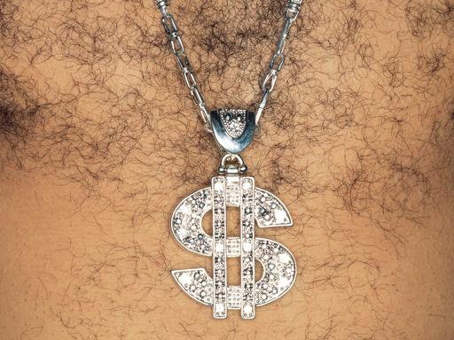 Ein Mann mit behaarter Brust, der ein glitzernde Kette mit einem US-Dollar-Zeichen als Anhänger trägt.
