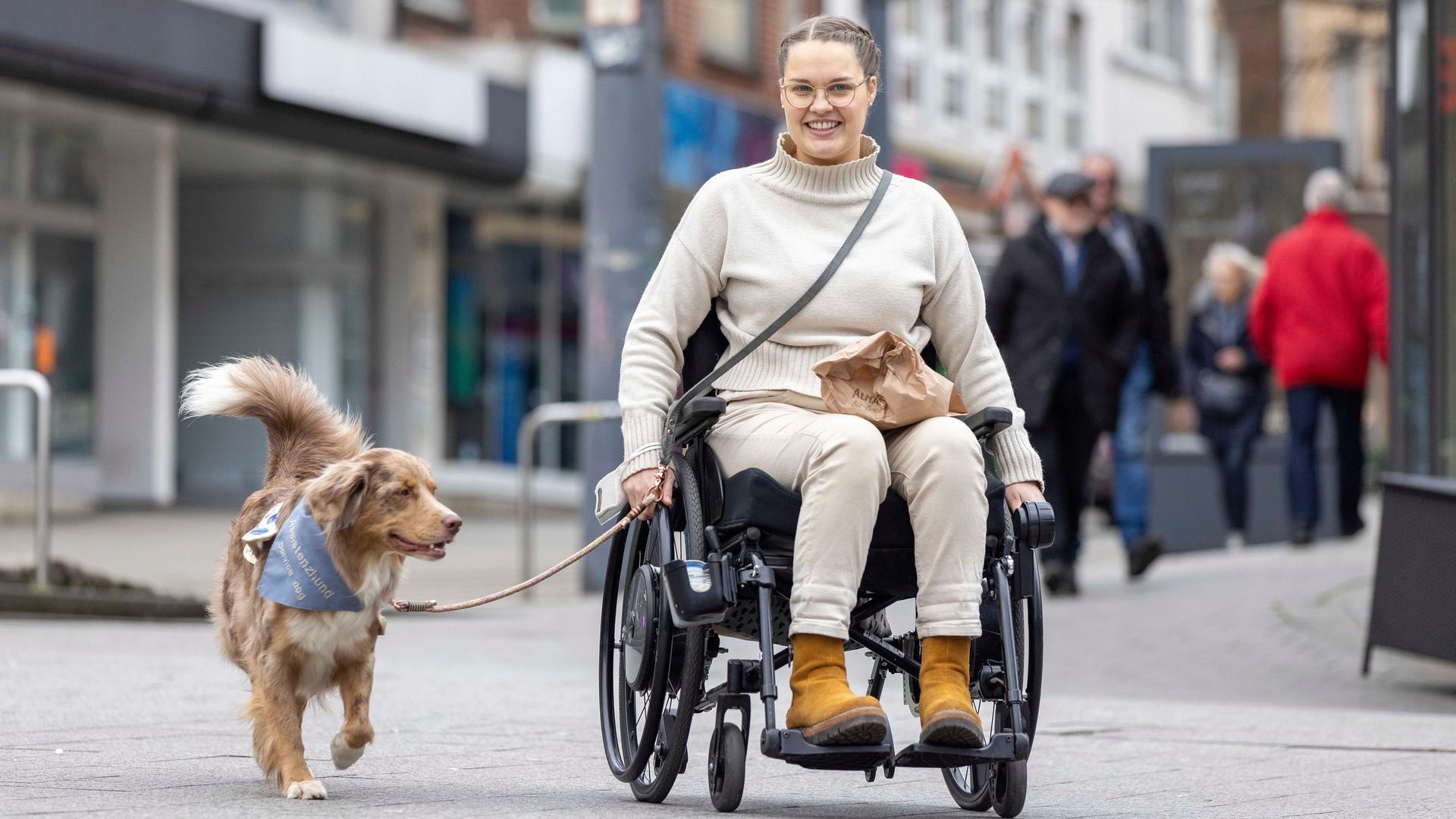 Eine Frau im Roll-Stuhl mit ihrem Assistenz-Hund in einer Innen-Stadt Eine Frau im Roll-Stuhl mit ihrem Assistenz-Hund in einer Innen-Stadt