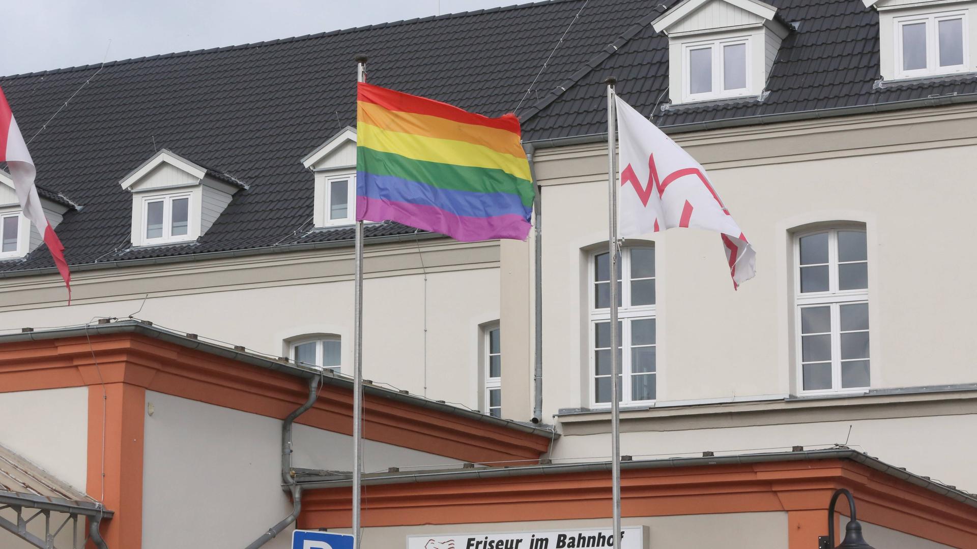 Die gehisste Regenbogenflagge vor den oberen Stockwerken und Dächern des Bahnhofsgebäude ist zu sehen.