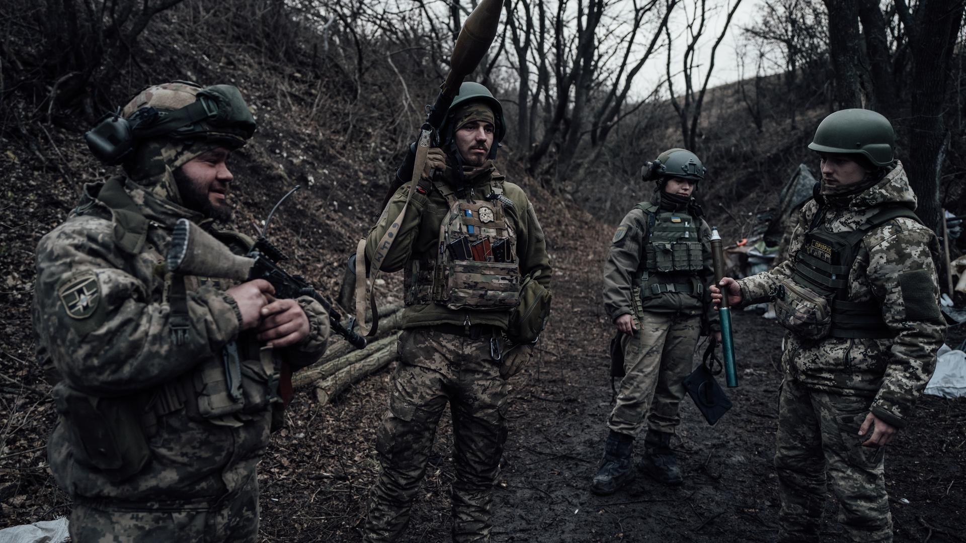 Vier Soldaten im Donbass stehen in einem Waldstück nebeneinander mit Artillerie. Im hinterrgrund sieht man eine Art Zelt. Copyright Adrien Vautier. März 2023.
